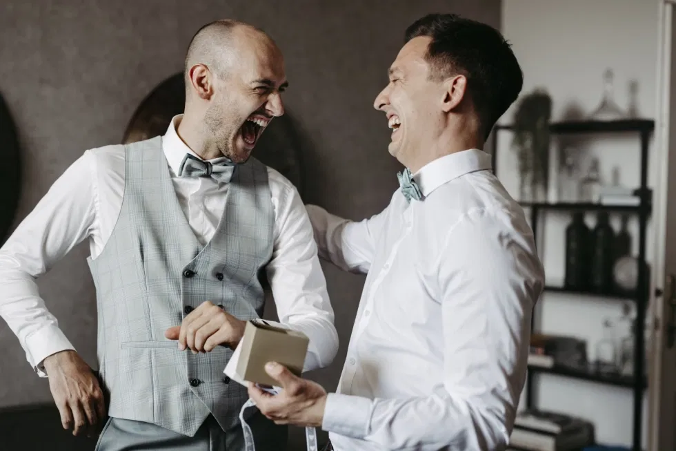 Zwei Männer in eleganter Hochzeitskleidung lachen herzlich beim Getting-ready.