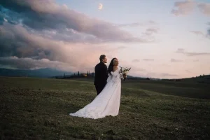 Brautpaar posiert in sanfter Abendstimmung auf weitem Feld unter dem Mond und sorgt für cineastische Hochzeitsmomente.
