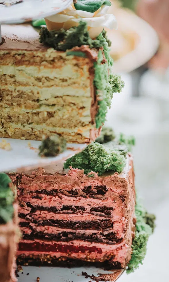 Anschnitt einer mehrschichtigen Hochzeitstorte mit farbigen Füllungen und grünen Dekoelementen.