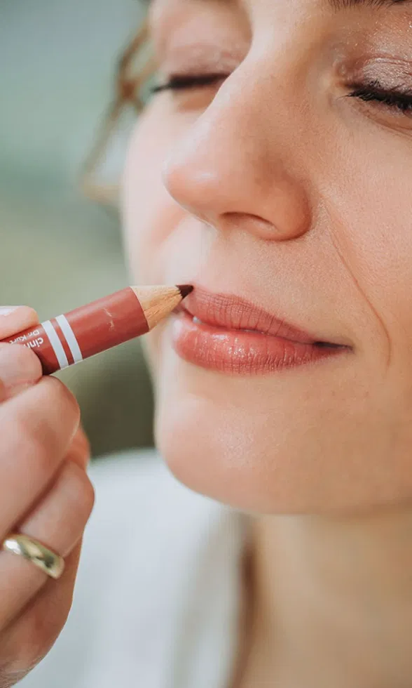 Detailaufnahme einer Hand, die sanft Lipliner auf die Lippen der Braut aufträgt.