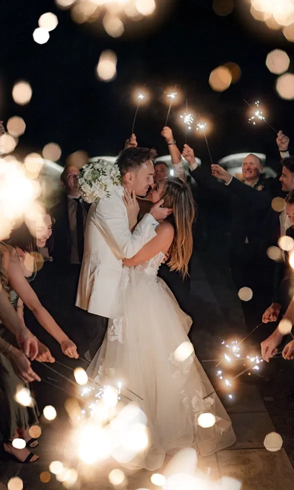 Braut und Bräutigam küssen sich beim funkelnden Spalier aus Wunderkerzen, umgeben von ihren Hochzeitsgästen.