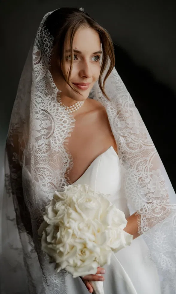 Elegantes Brautporträt mit Spitzen-Schleier und weißem Brautstrauß, das zeitlose Eleganz und Ruhe ausstrahlt.
