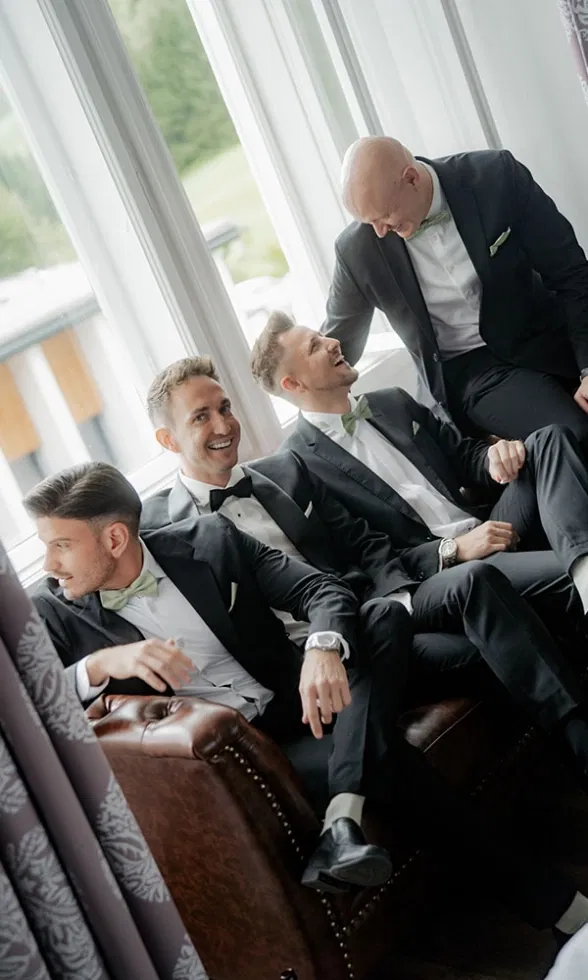 Bräutigam sitzt gemeinsam mit seinen Trauzeugen im Smoking auf einem Ledersofa, entspannte Stimmung vor der Hochzeit.
