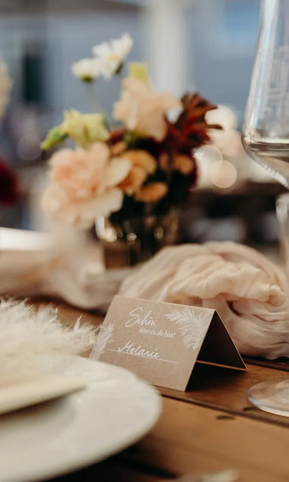 Stilvoll gedeckter Hochzeitstisch mit Namenskärtchen, feinen Stoffservietten und floraler Dekoration in warmen Naturtönen.
