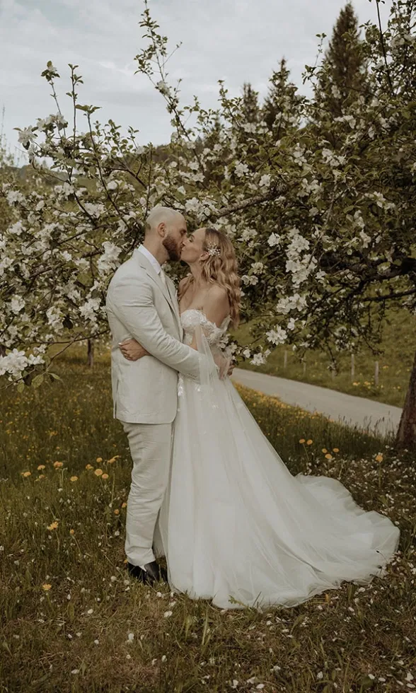 Romantisches Paarfoto: Das Hochzeitspaar teilt einen Kuss zwischen blühenden Zweigen auf einer Frühlingswiese.