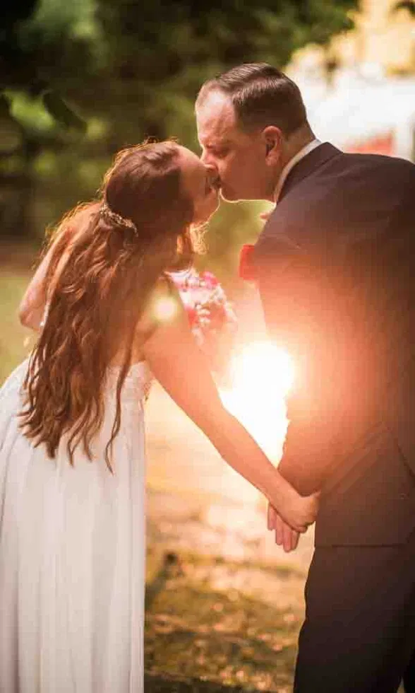Braut und Bräutigam küssen sich im warmen Licht der tief stehenden Sonne und halten dabei liebevoll Händchen.