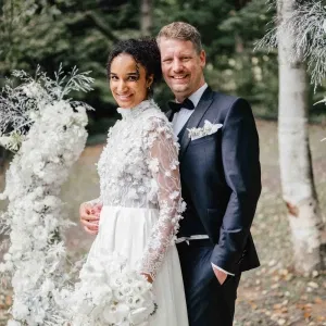 Brautpaar im Wald bei der Trauung, die Braut im langärmeligen Spitzenkleid mit weißen Schmetterlingsdetails, der Bräutigam im dunklen Anzug mit passendem Blumenanstecker.