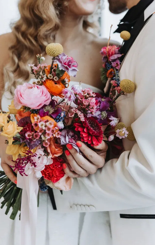 Brautpaar mit farbenfrohem Brautstrauß in Pink-, Orange- und Rottönen, passend zum Artsy Wedding Farbkonzept.