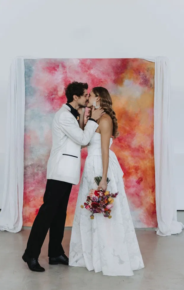 Brautpaar küsst sich vor abstrakter Leinwand als Trauhintergrund, emotionale Szene einer modernen Artsy Wedding.