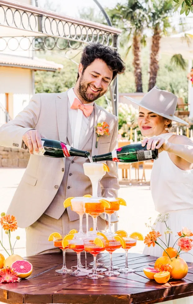 Brautpaar gießt Schaumwein in einen Aperol-Spritz-Turm – fröhlicher Aperitif bei der Tageshochzeit