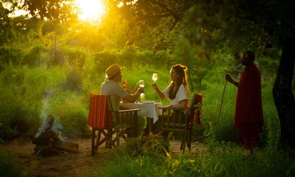 Romantisches Paar genießt ein privates Dinner im Grünen bei Sonnenuntergang in afrikanischer Naturkulisse.
