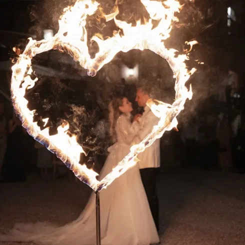 Brautpaar steht eng umschlungen in einem brennenden Herz aus Feuer.