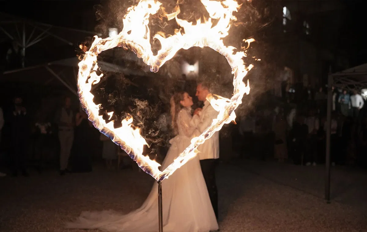 Brautpaar steht eng umschlungen in einem brennenden Herz aus Feuer.