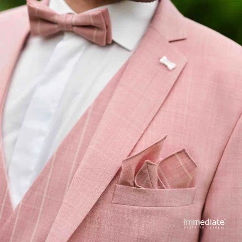 Detailaufnahme eines Bräutigams im roséfarbenen Anzug mit Fliege, Einstecktuch und feiner Reversnadel.