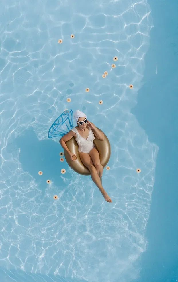Braut treibt entspannt auf einem Schwimmring im Pool, umgeben von Blüten – entspannte Me-Time in der Woche vor der Hochzeit.