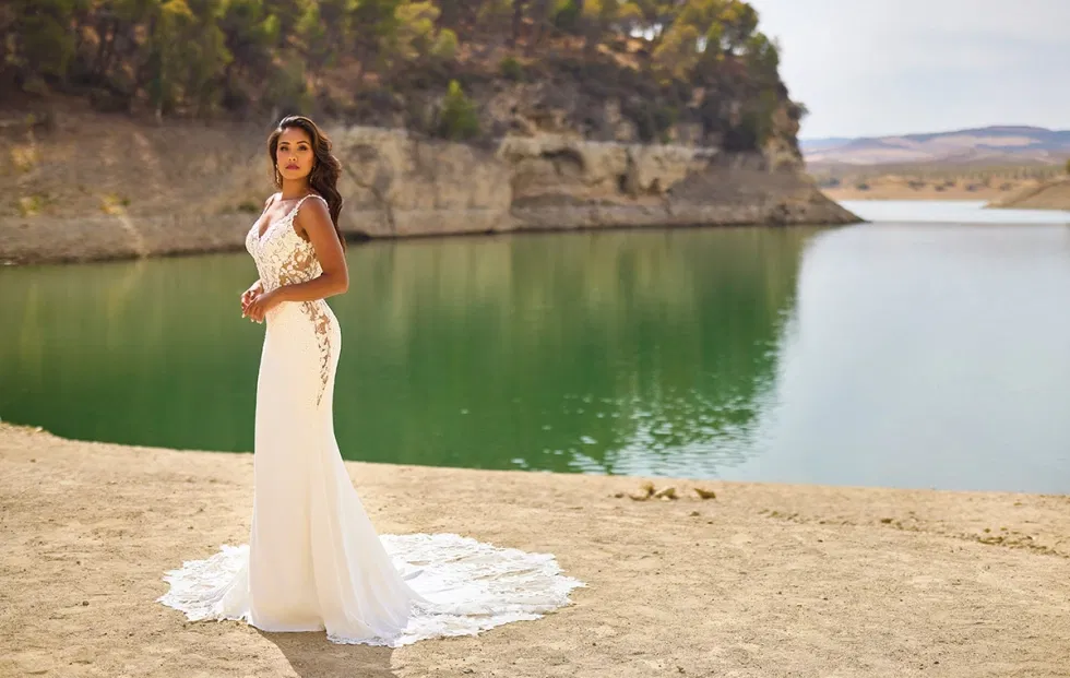 Schlichtes, figurbetontes Brautkleid mit Spitzendetails, inszeniert an einem See mit ruhiger Landschaft und natürlicher Weite.