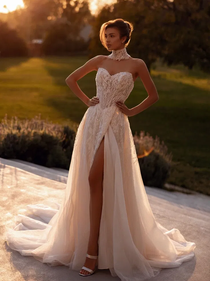 Glamouröses Brautkleid mit herzförmigem Ausschnitt, Choker-Detail und hohem Schlitz, aus zartem Tüll mit aufwendiger Stickerei im warmen Sonnenlicht.