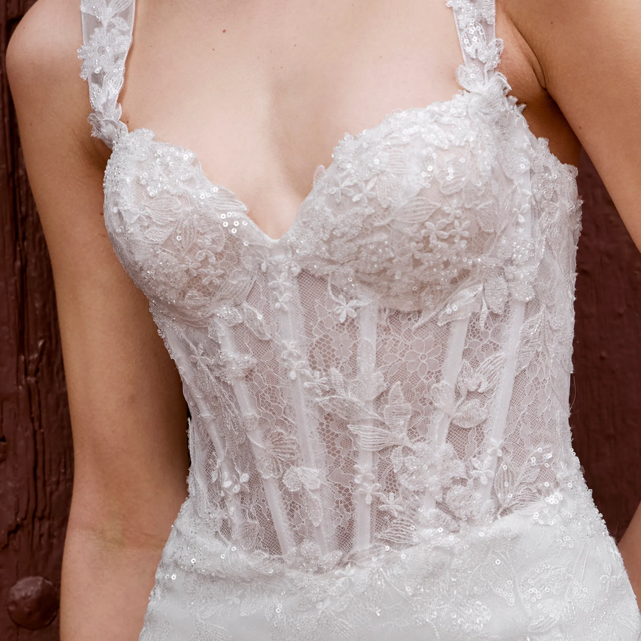 Detailaufnahme eines Brautkleides mit transparenter Corsage, floraler Spitze und zarten Trägern, verziert mit feinen Stickereien und schimmernden Perlenapplikationen.