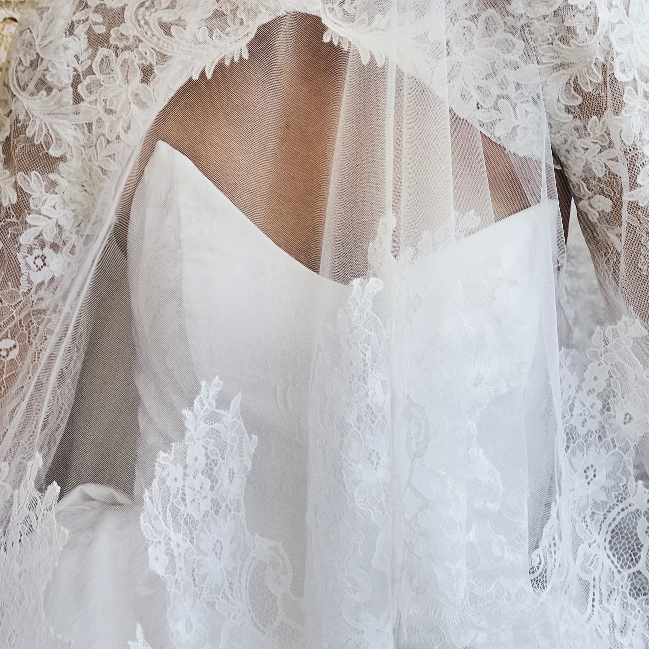 Detailaufnahme eines Brautkleides mit tiefem Rückenausschnitt, feiner Spitze und transparentem Schleier mit floralen Applikationen in Ivory.