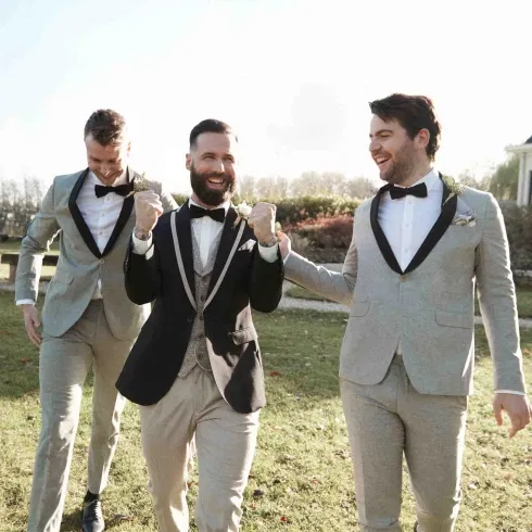 Bräutigam feiert ausgelassen mit seinen Trauzeugen im Garten, alle im Anzug und mit Fliege.