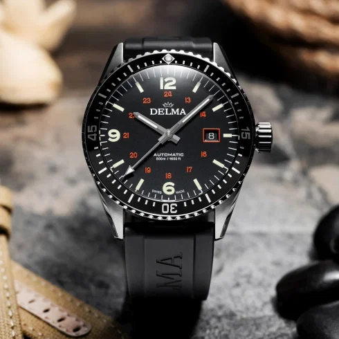 Schwarze Armbanduhr mit markantem Zifferblatt, Leuchtindizes und Datumsanzeige auf strukturiertem Untergrund