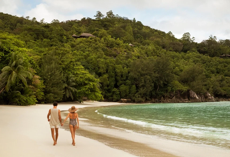 Paar spaziert Hand in Hand am Strand der Seychellen – unvergessliche Flitterwochen mit Constance Hotels & Resorts