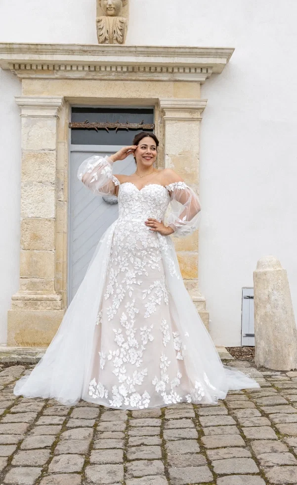 Braut in romantischem Brautkleid mit floraler Spitze und Off-Shoulder-Tüllärmeln vor historischer Kulisse