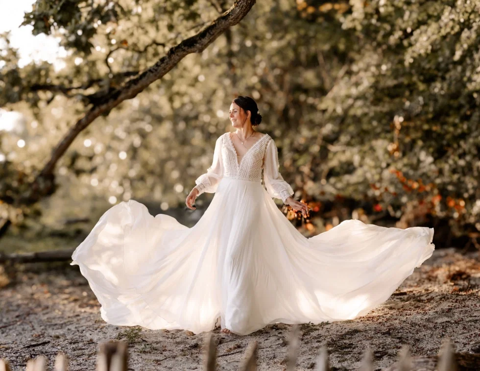Braut im fließenden Boho-Brautkleid bei einem romantischen Brautshooting im Wald am Wasser.