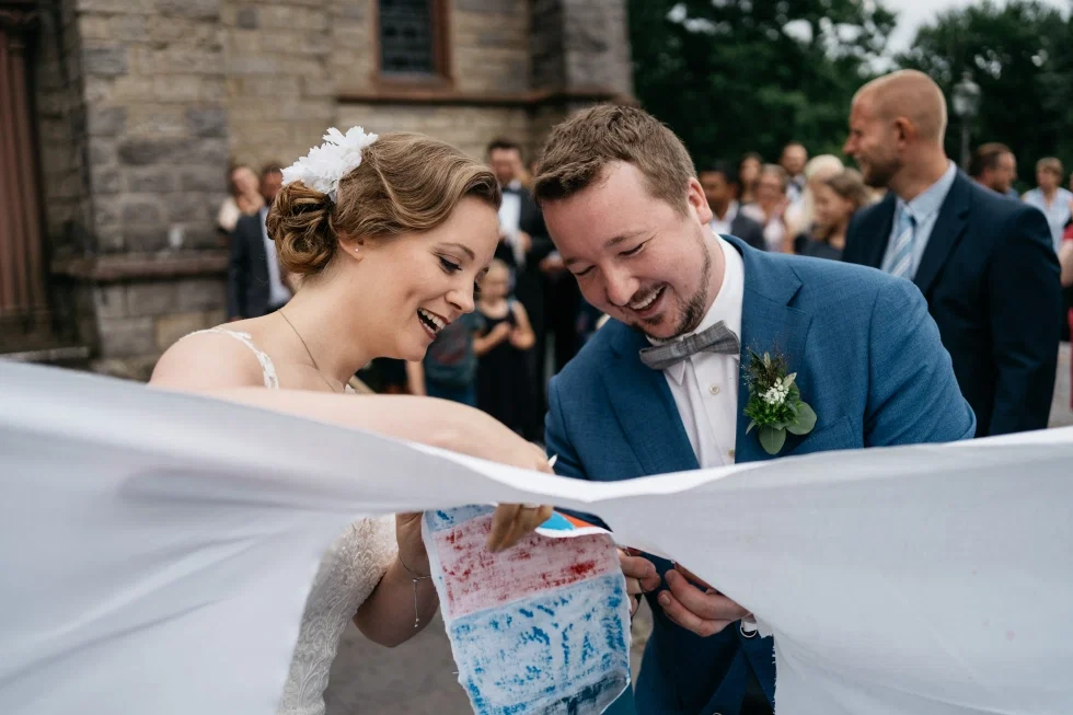 Janina und Sebastian durchschneiden ein Laken nach ihrer kirchlichen Trauung