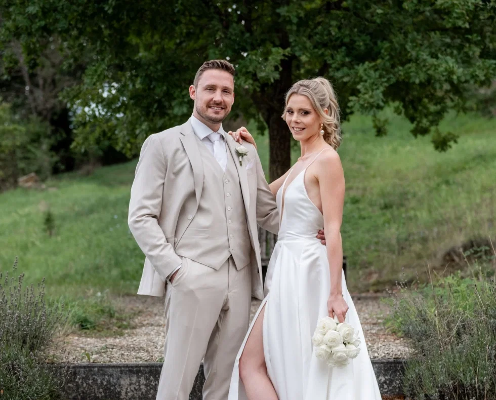 Pia und Tony in ihren Hochzeitsoutfits vor grüner Kulisse.