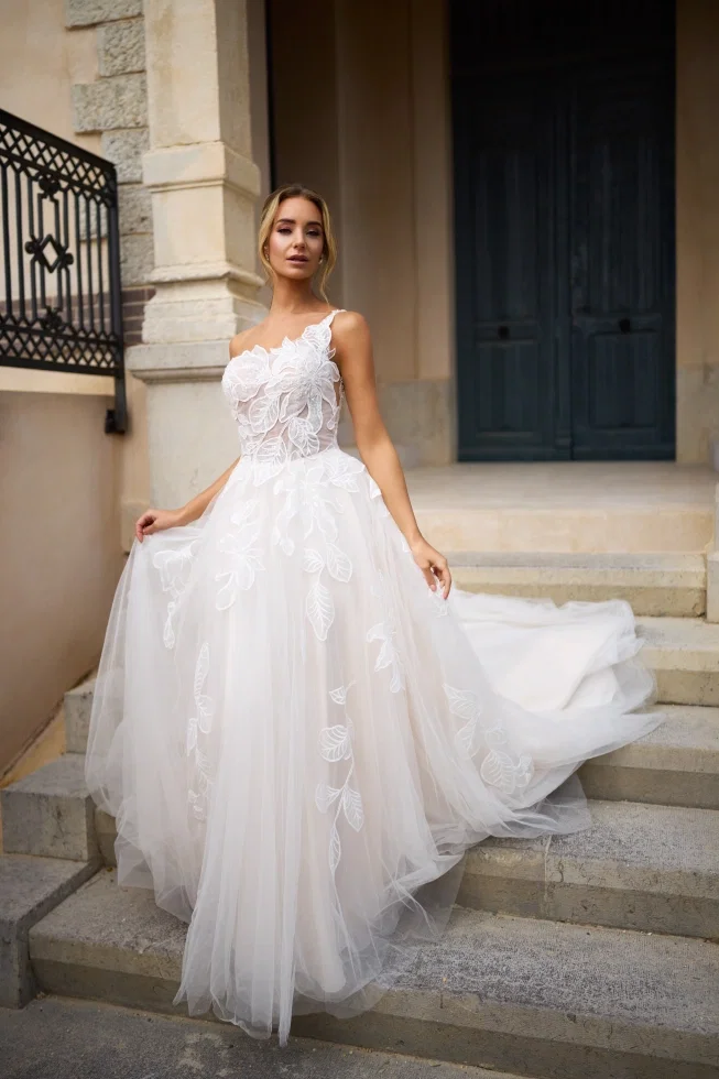 Dieses Kleid in A-Linie von Très Chic besticht durch ein asymmetrisches Mieder mit modernem One-Shoulder-Ausschnitt. Zarte Spitzenapplikationen verlaufen vom Oberteil hinab über den Rock.